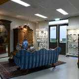 Kamer met kasten vol antieke spullen en een blauwe bank in het midden.